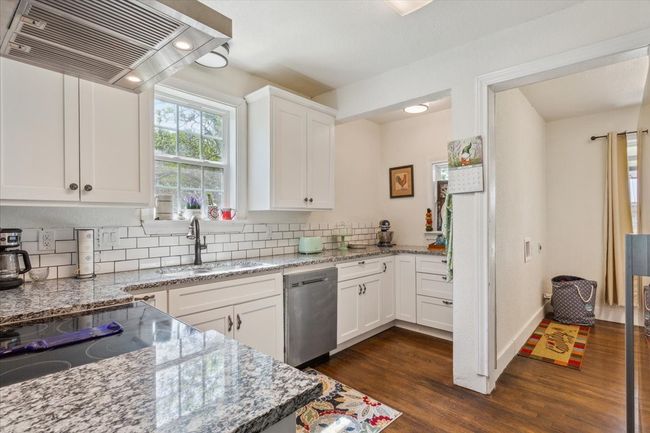 Kitchen with wall chimney range hood, backsplash, dark wood finished floors, stainless steel dishwasher, and a sink | Image 10