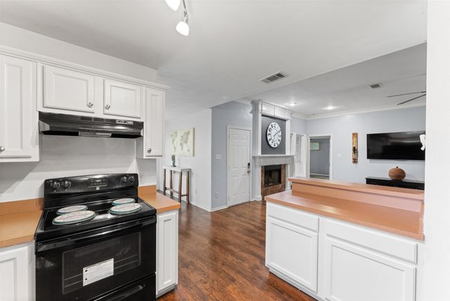 Kitchen with electric range, under cabinet range hood, light countertops, white cabinets, and crown molding | Image 12