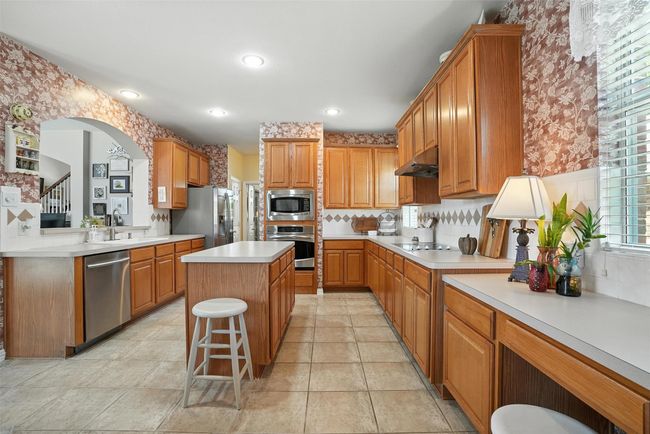 Kitchen featuring stainless steel appliances, under cabinet range hood, wallpapered walls, light countertops, and a kitchen island | Image 13