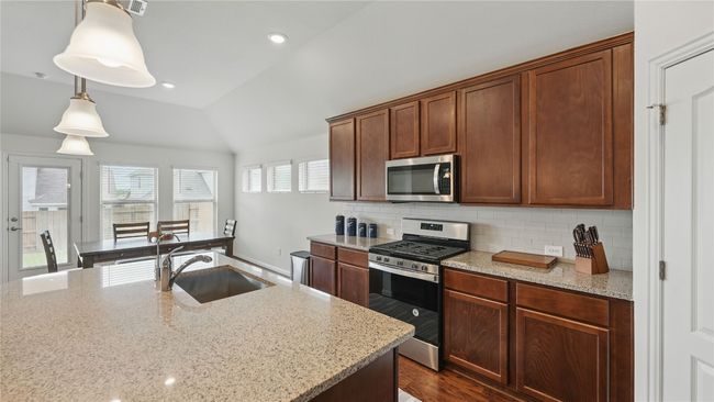 Kitchen with appliances with stainless steel finishes, lofted ceiling, tasteful backsplash, light stone counters, and hanging light fixtures | Image 10