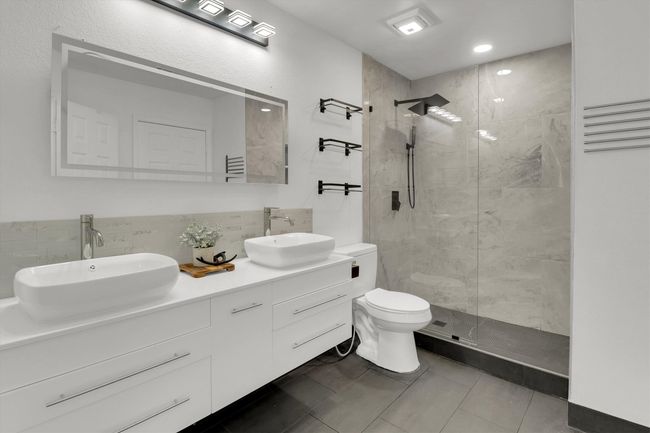 Bathroom with a shower stall, double vanity, dark tile patterned flooring, backsplash, and recessed lighting | Image 13