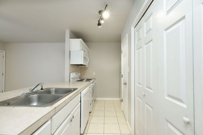 Kitchen with white appliances, white cabinetry, backsplash, light countertops, and light tile patterned floors | Image 8