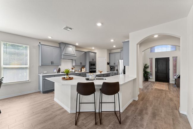 Kitchen with gray cabinets, custom exhaust hood, appliances with stainless steel finishes, arched walkways, and light wood-style floors | Image 7