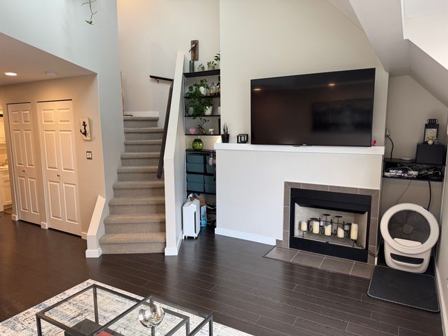 Living area with lofted ceiling, a tiled fireplace, wood finished floors, baseboards, and stairs | Image 10