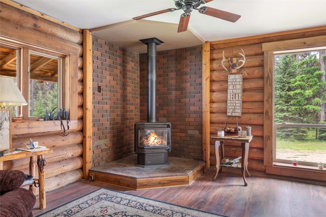 Living area featuring a wood stove, rustic walls, hardwood / wood-style flooring, and a ceiling fan | Image 33