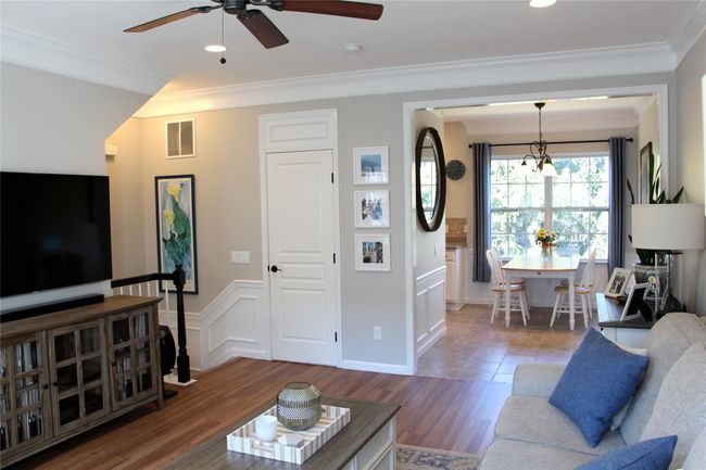 Living area with visible vents, crown molding, ceiling fan, a wainscoted wall, and wood finished floors | Image 6