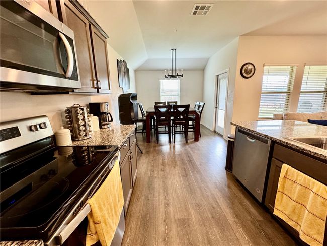 Kitchen with stainless steel appliances, wood finished floors, light stone counters, vaulted ceiling, and a chandelier | Image 4