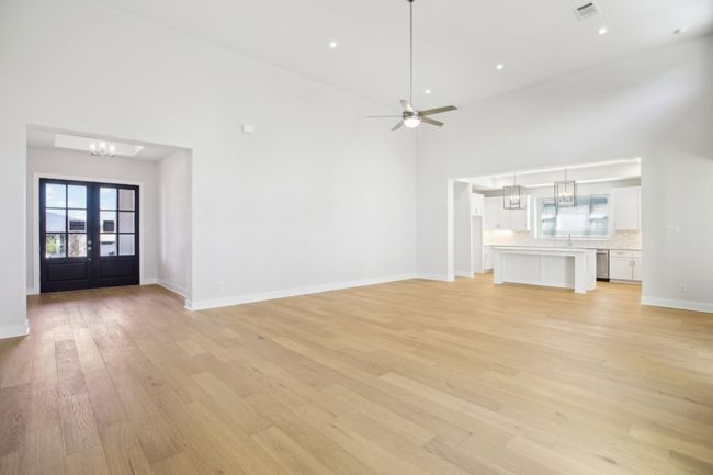 Unfurnished living room featuring ceiling fan with notable chandelier, a towering ceiling, visible vents, light wood finished floors, and baseboards | Image 6