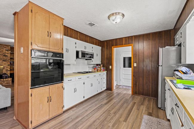 Kitchen with appliances with stainless steel finishes, a textured ceiling, light countertops, wood walls, and light wood-style flooring | Image 19