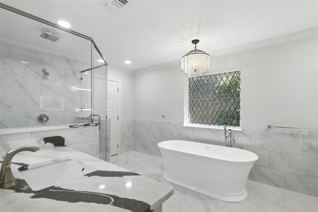 Bathroom featuring a marble finish shower, crown molding, a freestanding bath, tile walls, and a chandelier | Image 25