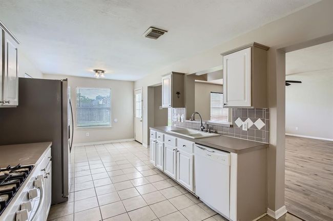 Light, bright kitchen has a small breakfast bar that opens up to family room. | Image 16