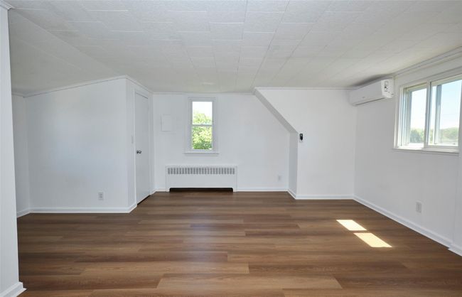 Bedroom with radiator heating unit, a wall mounted air conditioner, dark wood-style floors, and baseboards | Image 20