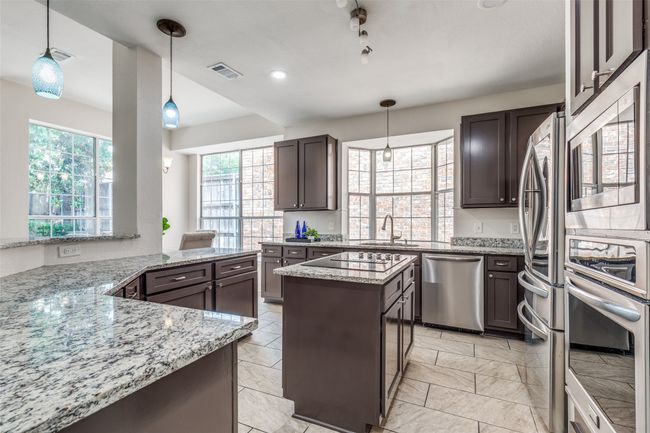 Kitchen featuring appliances with stainless steel finishes, a sink, a kitchen island, light stone counters, and dark brown cabinets | Image 10