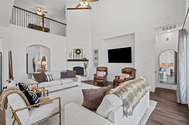 Living room featuring arched walkways, a high ceiling, ceiling fan, dark wood-style flooring, and a large fireplace | Image 4