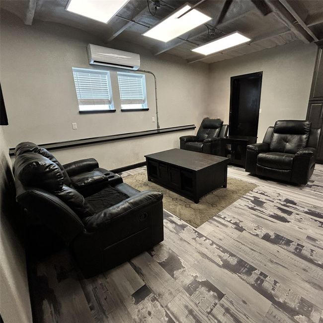 Cozy room with modern decor, featuring black leather recliners and a matching sofa. The space has ample lighting, a sleek coffee table, and air conditioning, creating a comfortable and inviting atmosphere. | Image 6