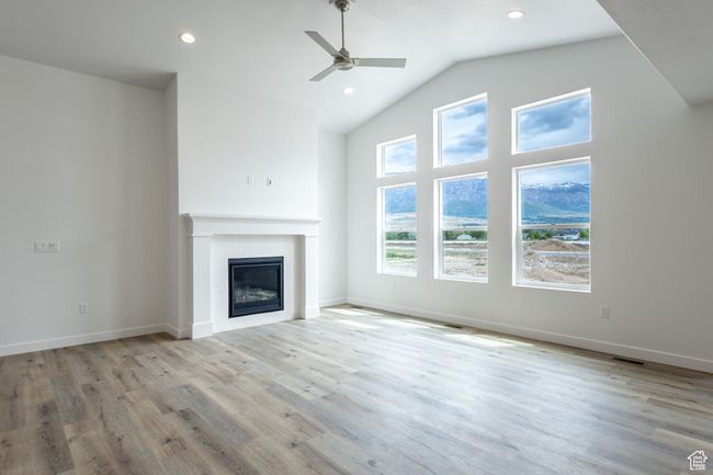 Unfurnished living room with ceiling fan, a glass covered fireplace, wood finished floors, recessed lighting, and baseboards | Image 6