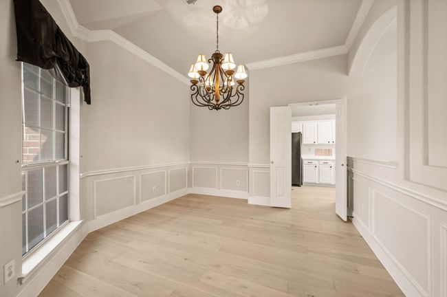 Unfurnished dining area featuring light wood finished floors, crown molding, a decorative wall, and an inviting chandelier | Image 7