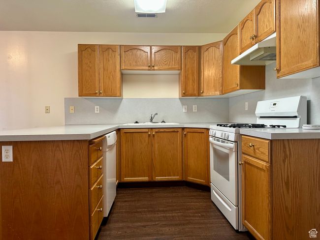Kitchen with white appliances, under cabinet range hood, dark wood-style floors, and light countertops | Image 10