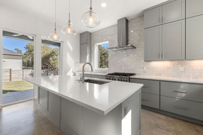 Kitchen with stove, a sink, gray cabinets, wall chimney exhaust hood, and finished concrete floors | Image 13