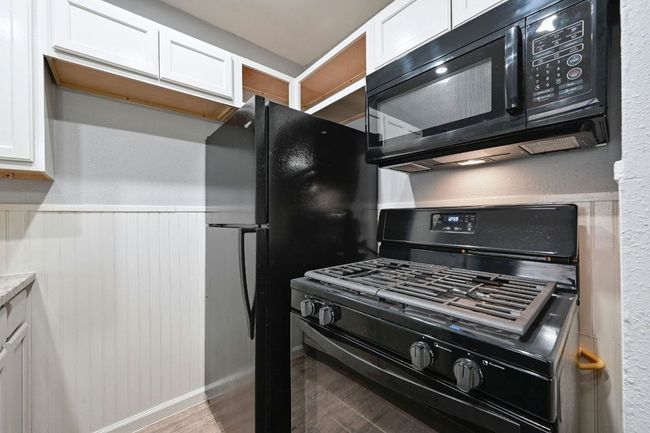 Kitchen with black appliances, white cabinets, light wood-style flooring, wainscoting, and a textured wall | Image 14