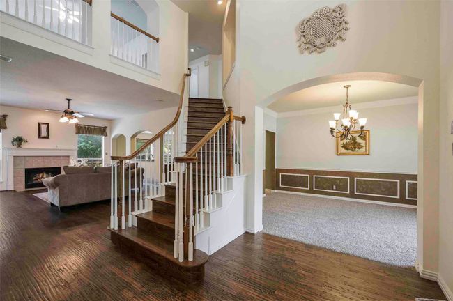 Staircase featuring a high ceiling, a tiled fireplace, arched walkways, wood finished floors, and ceiling fan with notable chandelier | Image 4