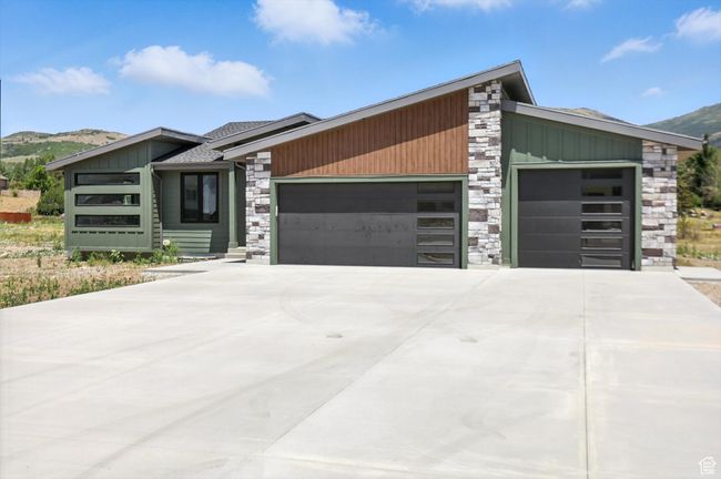 View of front facade featuring stone siding, a garage, board and batten siding, a mountain view, and concrete driveway | Image 58