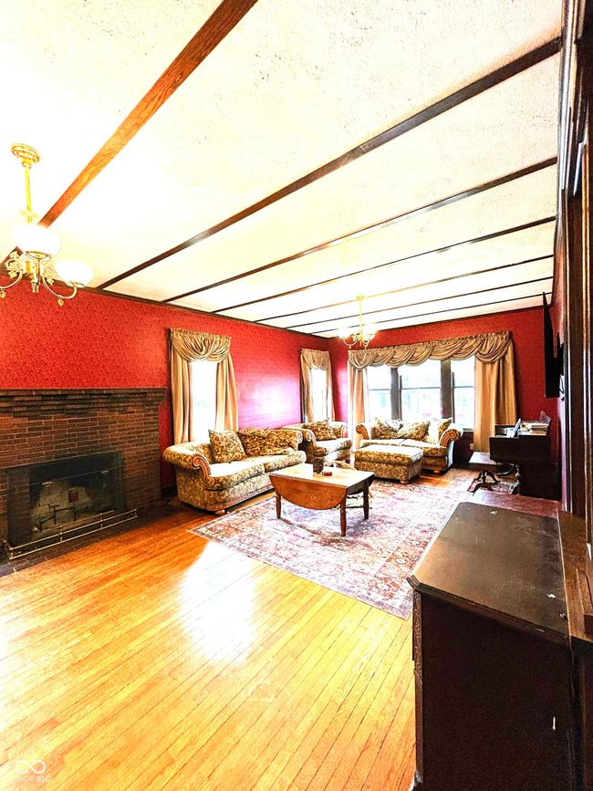 living area with beam ceiling, wood-type flooring, a chandelier, and a brick fireplace | Image 11