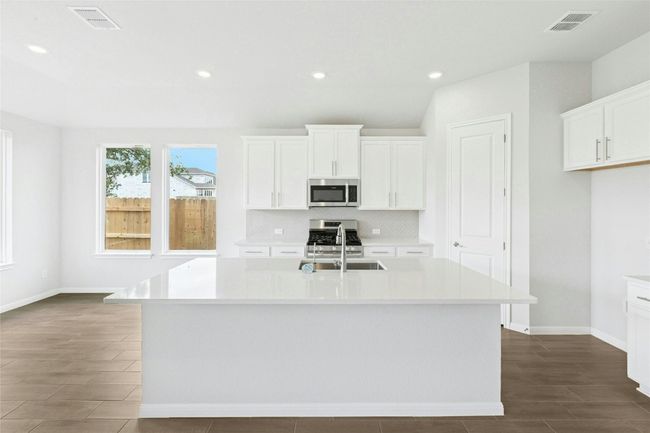 Kitchen featuring stainless steel microwave, a sink, tasteful backsplash, light countertops, and an island with sink | Image 6
