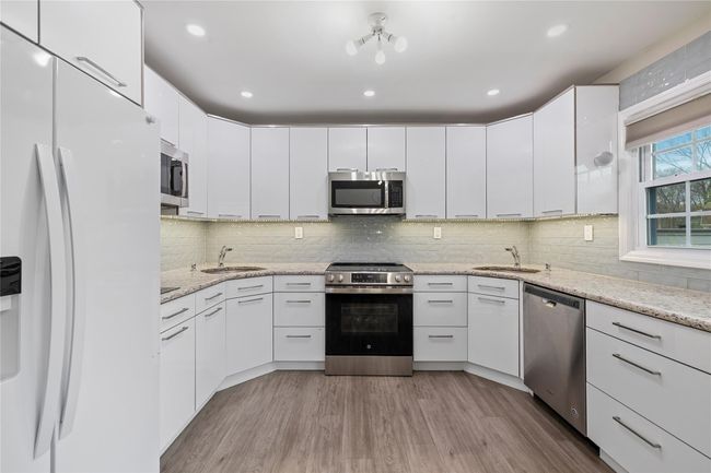 Kitchen featuring light wood finished floors, stainless steel appliances, a sink, and white cabinetry | Image 15