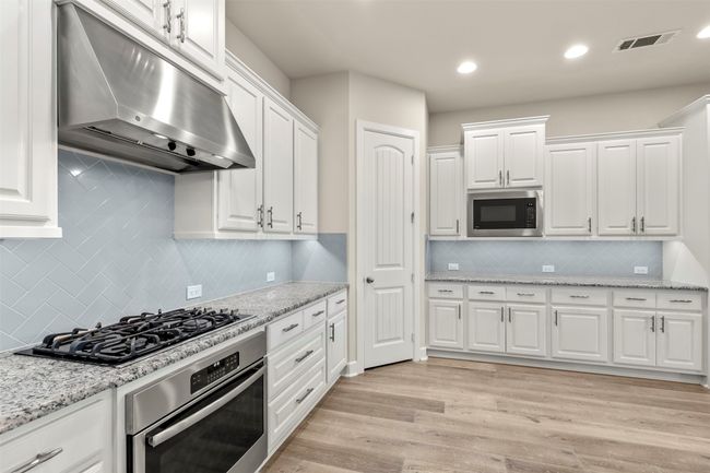 Kitchen featuring stainless steel appliances, under cabinet range hood, tasteful backsplash, white cabinetry, and recessed lighting | Image 9