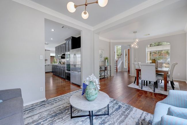 Living area featuring a chandelier, baseboards, dark wood-style flooring, crown molding, and stairs | Image 8