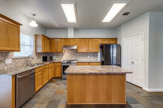 Kitchen featuring stainless steel appliances, under cabinet range hood, stone finish floors, a kitchen island, and backsplash | Image 13