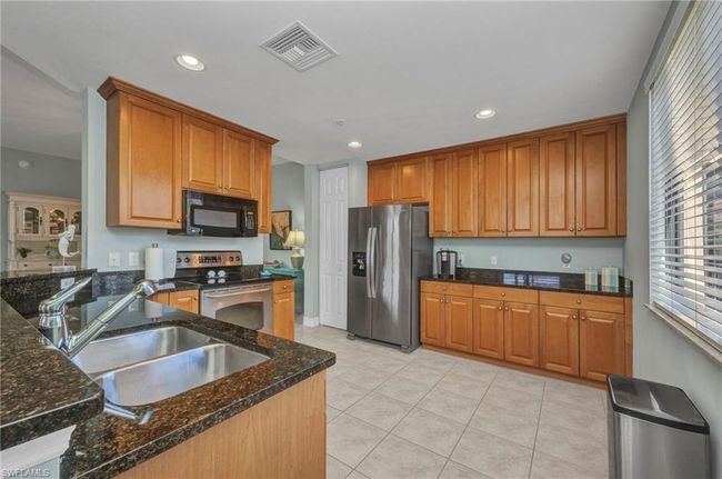 Kitchen featuring stainless steel appliances, recessed lighting, light tile patterned floors, dark stone countertops, and brown cabinets | Image 16