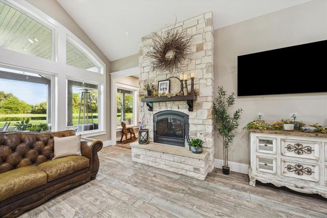 The living room is anchored by a floor-to-ceiling stone double-sided gas fireplace, featuring a natural stone hearth that adds warmth and elegance to the space, creating a striking focal point that enhances both style and comfort. | Image 12
