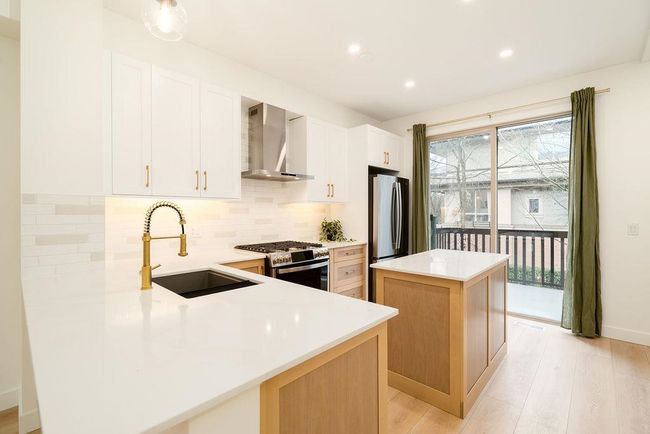 Kitchen with wall chimney exhaust hood, tasteful backsplash, appliances with stainless steel finishes, a sink, and a center island | Image 4
