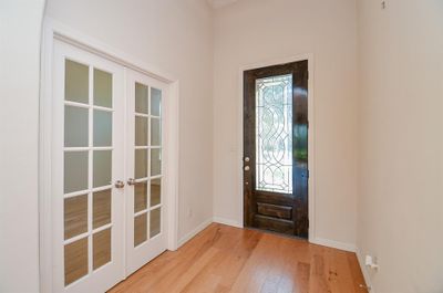 The bright entrance, from the inside, is bathed in pale neutral tones, shining hardwood floors; offering a beautiful private study/home office (left) behind classic french doors. | Image 3