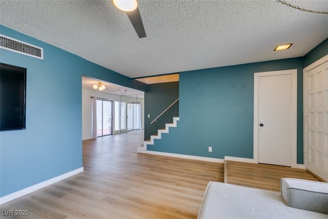 Living area with a textured ceiling, ceiling fan, wood finished floors, and stairway | Image 10