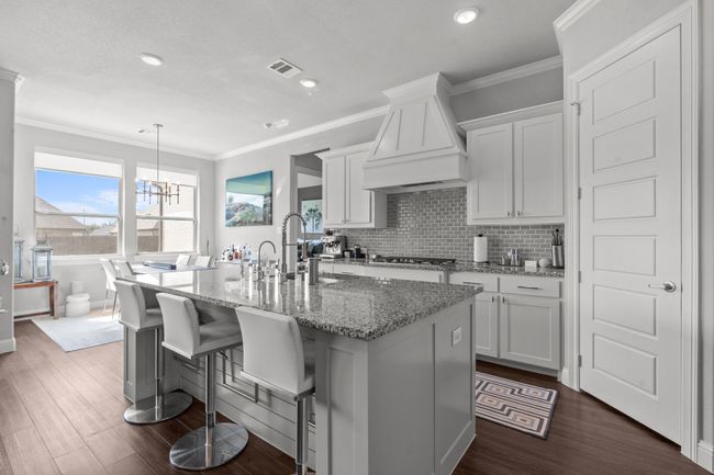 Kitchen featuring premium range hood, a center island with sink, white cabinets, dark wood finished floors, and crown molding | Image 5