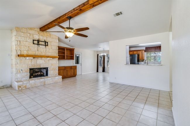 Unfurnished living room featuring visible vents, lofted ceiling with beams, a stone fireplace, ceiling fan with notable chandelier, and light tile patterned flooring | Image 23
