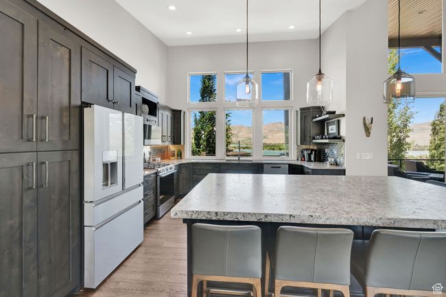 Kitchen featuring GE Cafe Platinum Glass refrigerator with ice dispenser, gas range, a sink, a kitchen breakfast bar, and decorative backsplash | Image 22