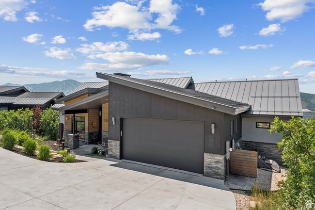 Contemporary house with a standing seam roof, an attached garage, a metal roof, driveway, and stone siding | Image 72