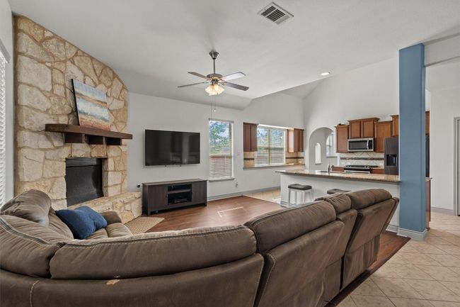 Living area featuring a ceiling fan, vaulted ceiling, light tile patterned flooring, a stone fireplace, and arched walkways | Image 8