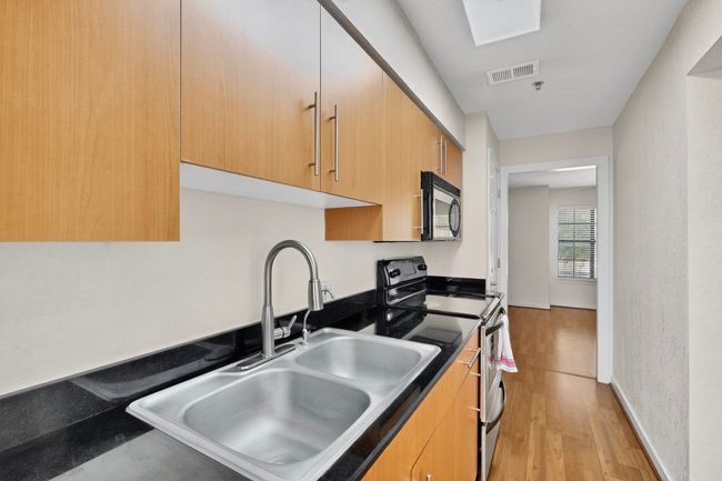 Kitchen featuring dark countertops, stainless steel range, light wood-style floors, black microwave, and light brown cabinetry | Image 19