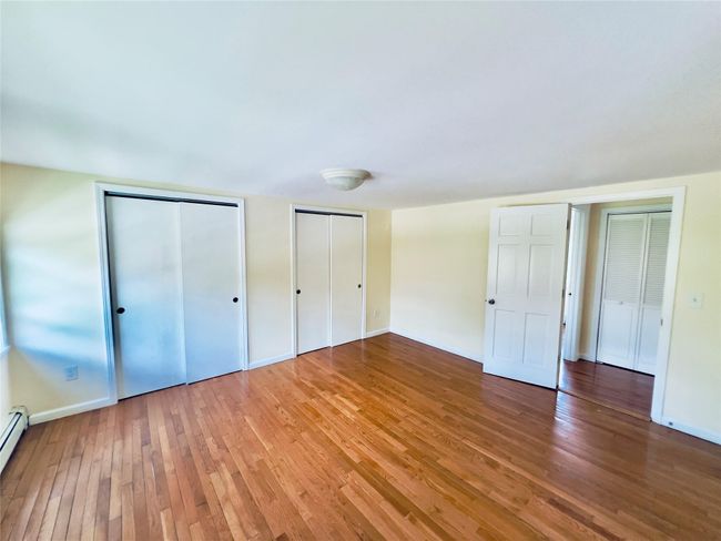 Unfurnished bedroom featuring light wood-style flooring, multiple closets, and a baseboard heating unit | Image 13