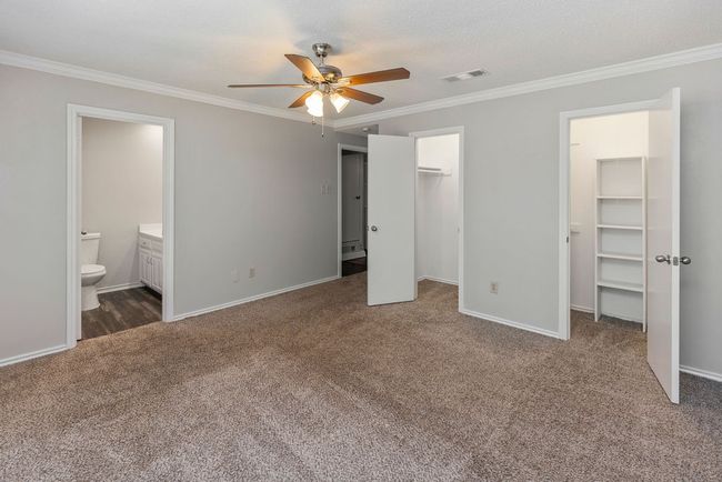 Unfurnished bedroom with a spacious closet, carpet flooring, crown molding, baseboards, and connected bathroom | Image 17