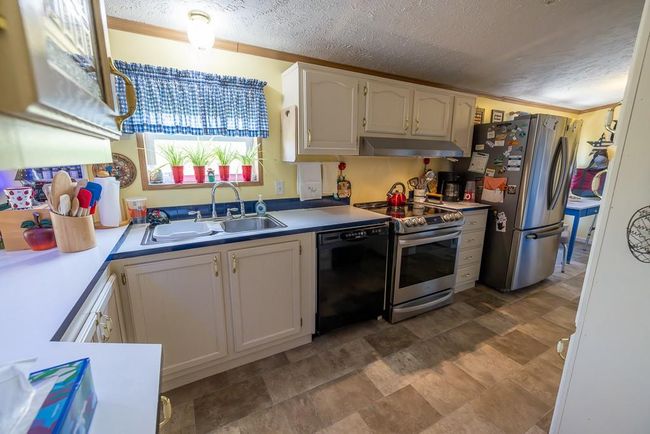 Kitchen with appliances with stainless steel finishes, a textured ceiling, under cabinet range hood, and a sink | Image 5