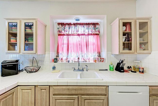 Kitchen featuring a sink, dishwashing machine, light brown cabinets, backsplash, and glass insert cabinets | Image 21