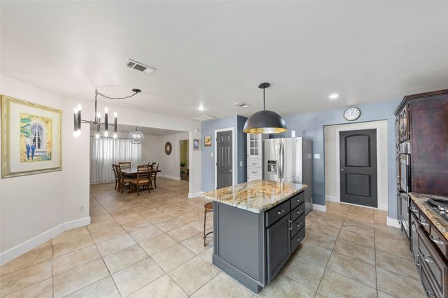 Kitchen with stainless steel appliances, light tile patterned flooring, a kitchen bar, visible vents, and light stone counters | Image 21