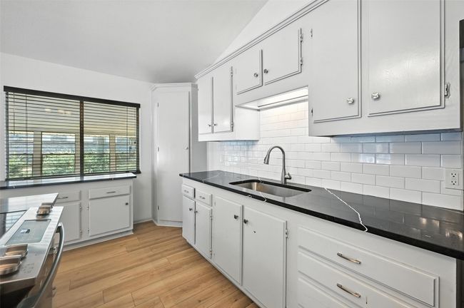 Kitchen with dark countertops, tasteful backsplash, white cabinetry, light wood-style flooring, and lofted ceiling | Image 11
