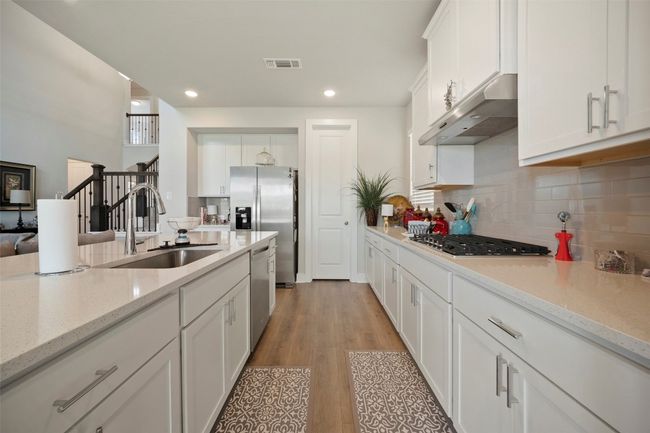 Kitchen featuring under cabinet range hood, appliances with stainless steel finishes, white cabinets, tasteful backsplash, and light wood-style flooring | Image 19